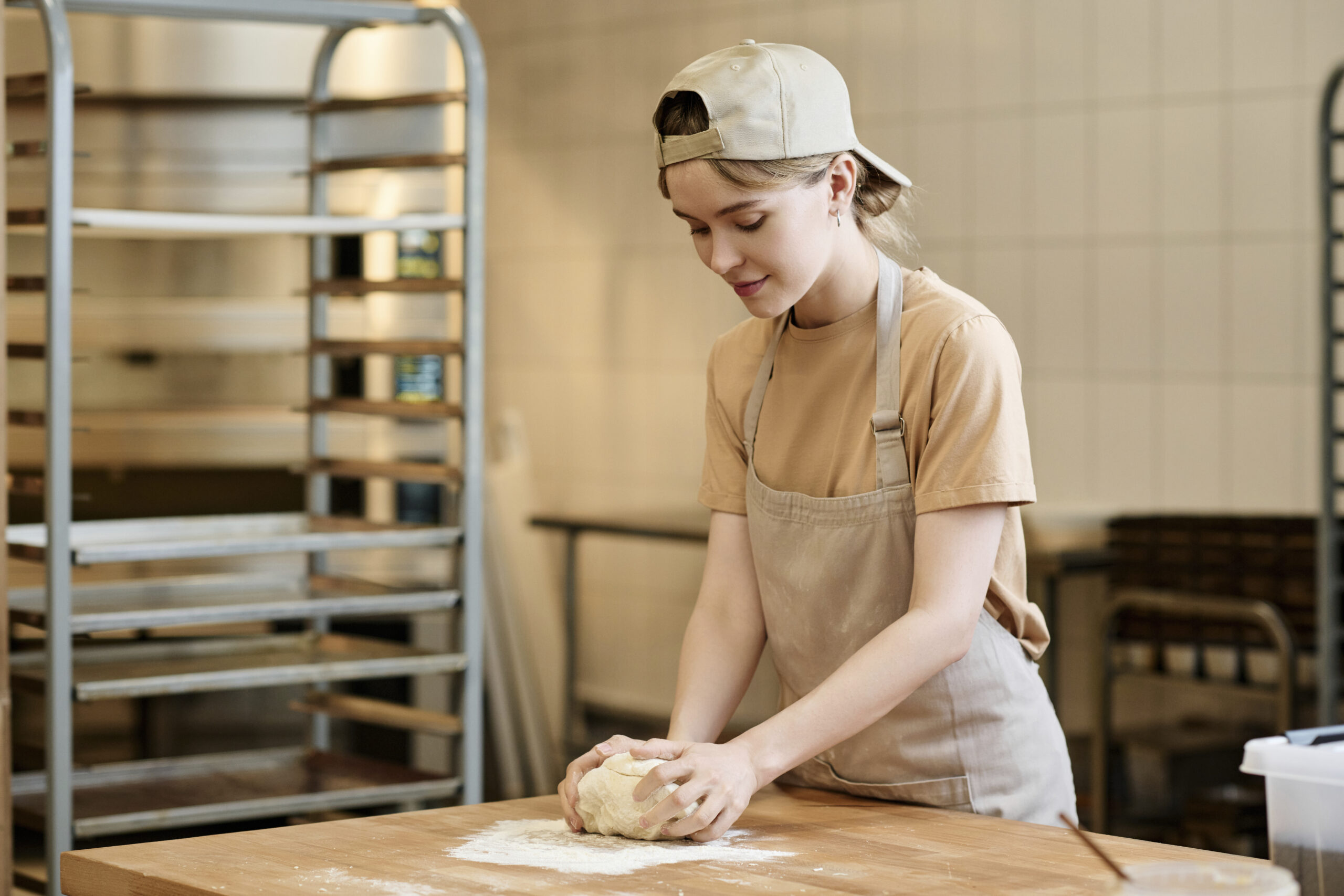 Smiling young woman kneading dough working in artisan bakery